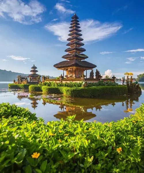 Temple de Pura Ulun Danu Bratan à Bali avec reflet sur l'eau, entouré de végétation luxuriante sous un ciel bleu clair, représentant la tranquillité culturelle